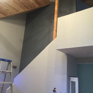 Interior of a room with a sloped wall, wooden beams, and a ladder, awaiting paint.