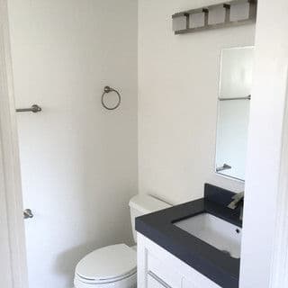 Modern bathroom with white walls, dark countertop, toilet, and minimalist fixtures.