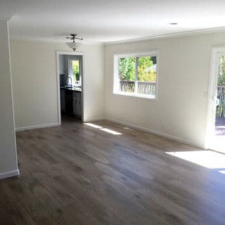 Bright, airy living room with wood-like flooring and large windows showcasing outdoor view.