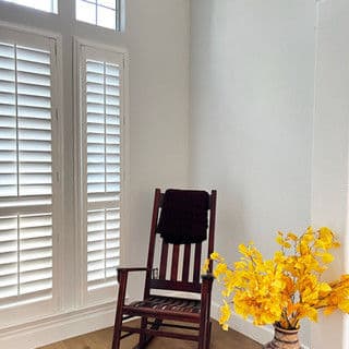 Cozy corner with a wooden rocking chair and vibrant yellow flowers in a vase.