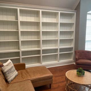 Modern living room with a large white bookshelf, brown sofa, and cozy chair.