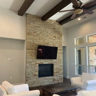 Modern living room featuring a stone accent wall, fireplace, and ceiling fan.