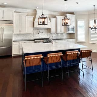 Modern kitchen with white cabinets, marble island, and brown leather bar stools.