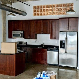 Modern kitchen with dark wood cabinets, stainless steel appliances, and concrete flooring.