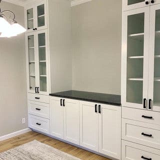 Modern white cabinetry with glass doors and black handles in a light-filled room.