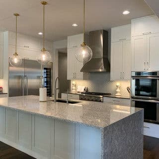 Modern kitchen with marble island, pendant lights, stainless steel appliances, and sleek cabinetry.