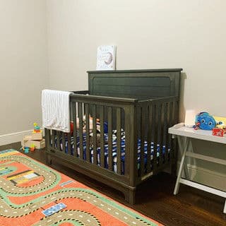 Modern nursery with a wooden crib, colorful rug, and toys on a side table.