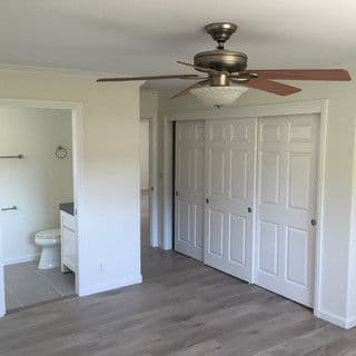 Spacious bedroom with ceiling fan, closet doors, and light-colored walls.