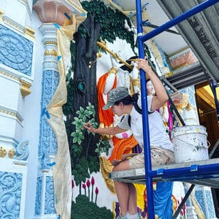 Artist painting a mural on scaffolding, featuring vibrant figures and lush greenery.