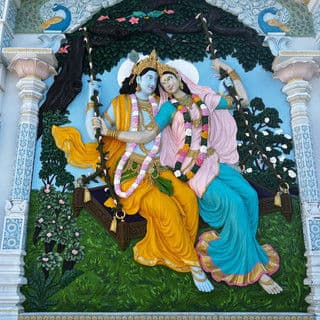 Vibrant mural of Radha and Krishna swinging in a lush garden setting. Colorful floral details.