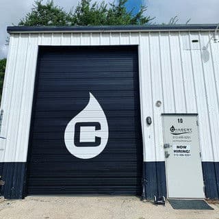 Exterior of a warehouse featuring a large logo and a "Now Hiring" sign.