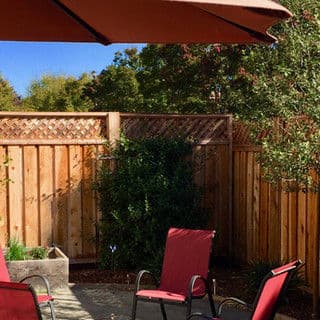 Outdoor patio with red chairs, wooden fence, and sunny blue sky in the background.