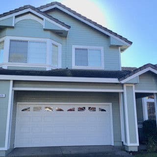 Two-story light blue house with a white garage door and large front windows.