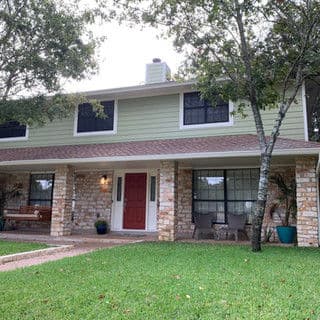 Two-story green house with stone accents, red door, and lush green front yard.