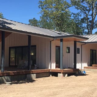 Modern home exterior with metal roof and wooden deck in a sunny outdoor setting.