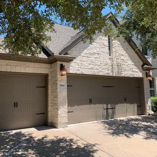 Two-car garage with stone facade and decorative wall lights surrounded by lush trees.