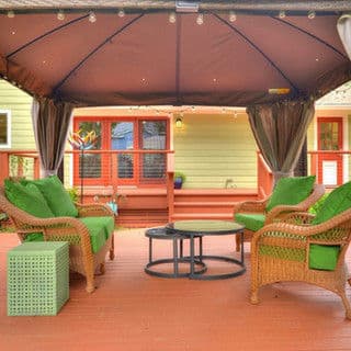 Cozy outdoor seating area with green cushions under a gazebo, surrounded by wooden deck.