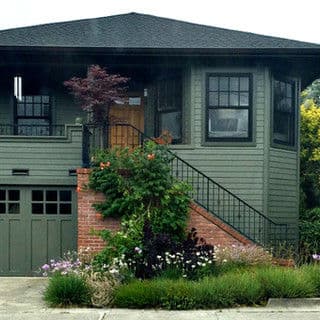 Green house with a staircase, brick accents, and lush landscaping in front.