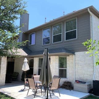 Modern two-story house with stone accents and patio furniture in a sunny backyard.