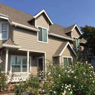 Exterior of a two-story house featuring a gray facade and blooming rose bushes in the foreground.