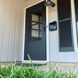 Modern black front door with window, welcoming porch, and green grass.