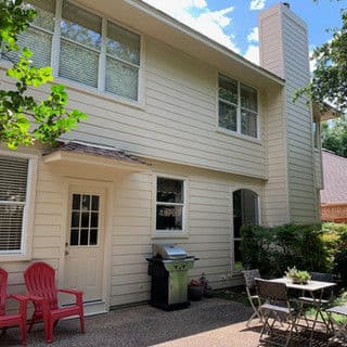 Modern two-story house exterior with a patio, grill, and outdoor seating area.