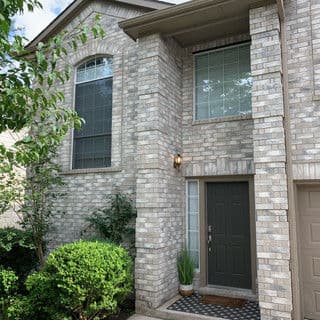 Modern brick house entrance with large windows, dark front door, and greenery.