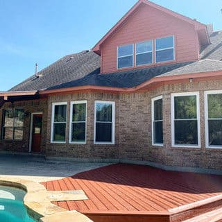 Beautiful brick home with large windows, red accents, and a poolside deck.