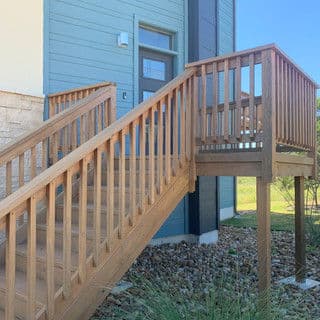 Wooden staircase leading to a blue building with a door, surrounded by grass and rocks.